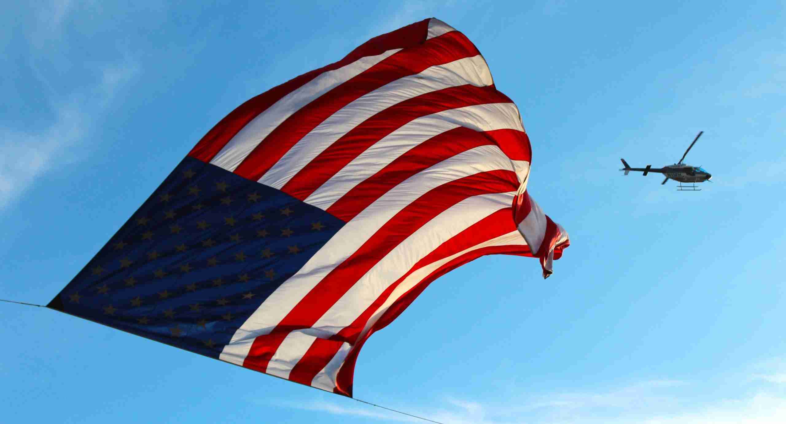 Massive US Flag Waves as Helicopters Patrol in Tense Skies